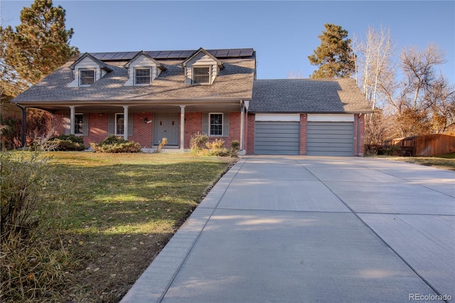 cape cod home featuring a garage, covered porch, a front yard, and solar panels