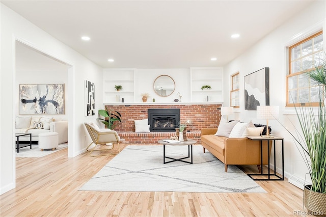 living room featuring a fireplace, built in shelves, and light hardwood / wood-style flooring