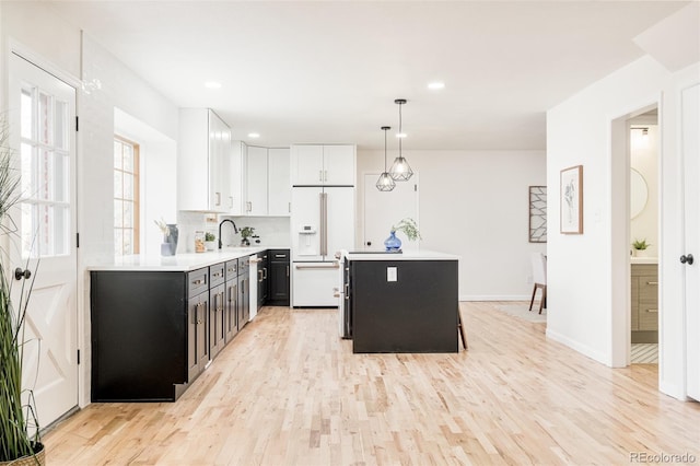 kitchen with white cabinetry, decorative backsplash, white built in fridge, decorative light fixtures, and light wood-type flooring