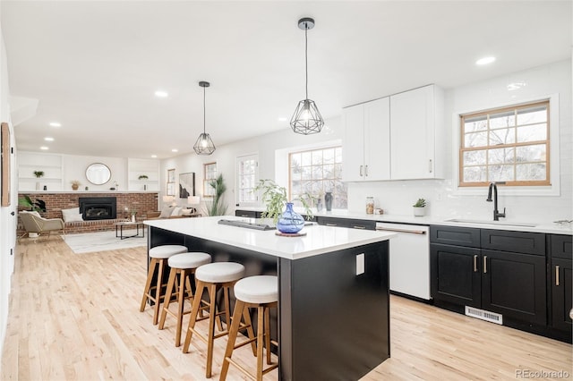 kitchen featuring sink, dishwasher, a kitchen island, pendant lighting, and white cabinets