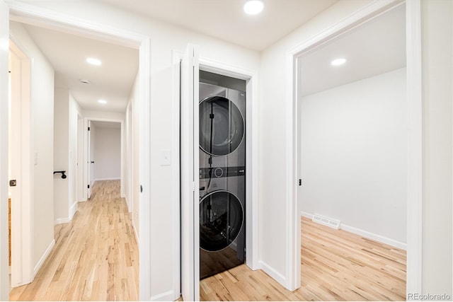 laundry area featuring stacked washer and clothes dryer and light hardwood / wood-style floors