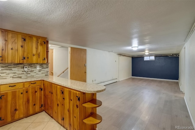 6095 W 47th Ave, Wheat Ridge, CO 80033 - kitchen with light countertops, a baseboard radiator, tasteful backsplash, brown cabinets, and a textured ceiling