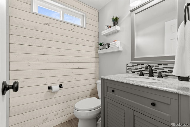 bathroom with wood walls, tasteful backsplash, hardwood / wood-style flooring, vanity, and toilet