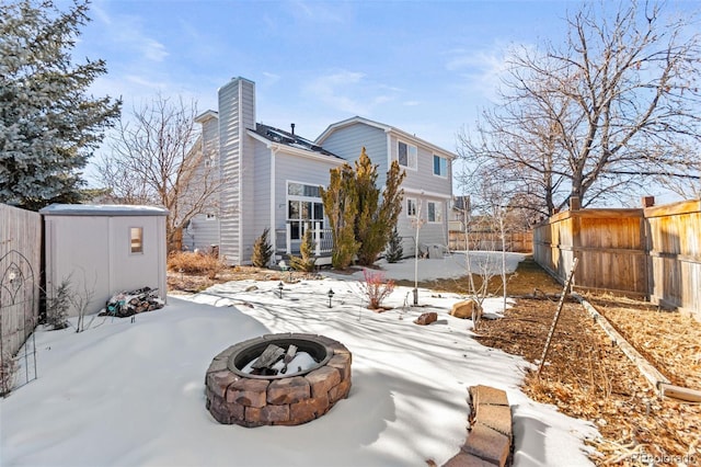 snow covered back of property featuring a shed and an outdoor fire pit