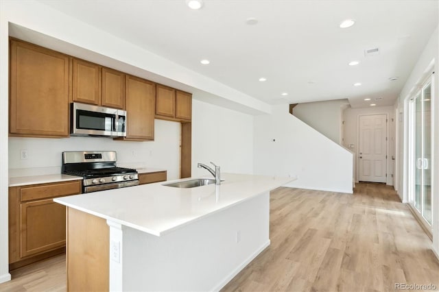 kitchen with sink, an island with sink, light wood-type flooring, and appliances with stainless steel finishes