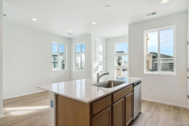 kitchen with light hardwood / wood-style flooring, stainless steel dishwasher, a kitchen island with sink, and sink