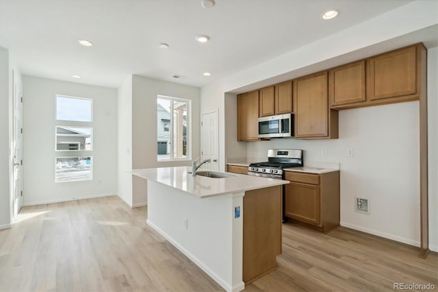 kitchen with sink, an island with sink, light wood-type flooring, and appliances with stainless steel finishes