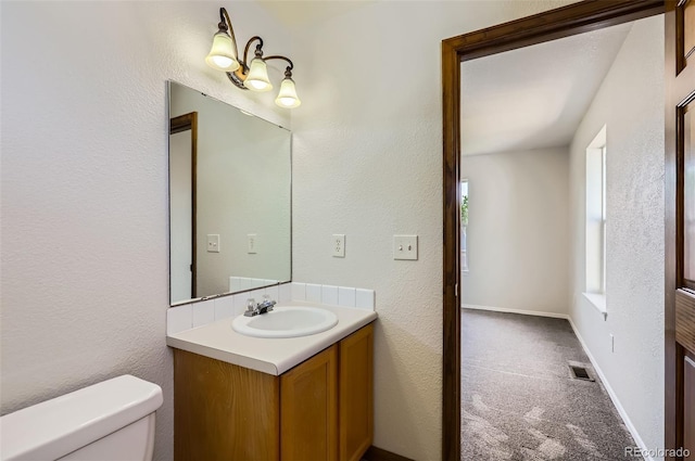 half bathroom featuring toilet, vanity, and a textured wall