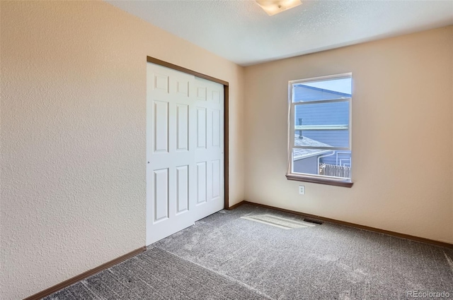 unfurnished bedroom featuring carpet floors, a closet, baseboards, and a textured wall