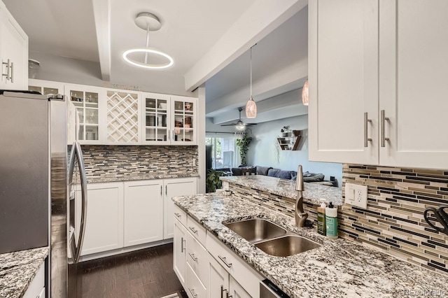 kitchen with stainless steel refrigerator with ice dispenser, hanging light fixtures, sink, white cabinetry, and light stone countertops