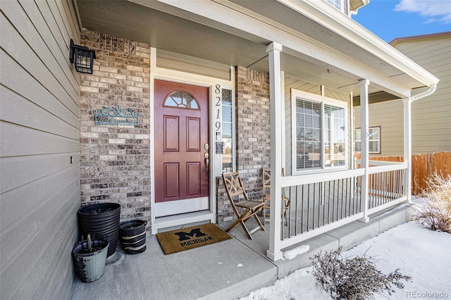 snow covered property entrance with covered porch and brick siding