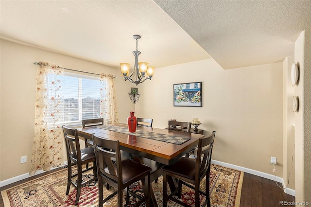 dining area with a textured ceiling, dark wood-type flooring, a notable chandelier, and baseboards