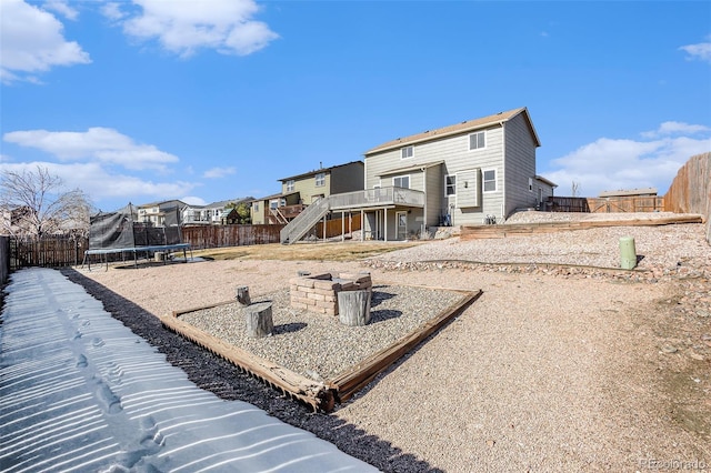 back of property featuring a fire pit, a fenced backyard, a residential view, a trampoline, and stairs