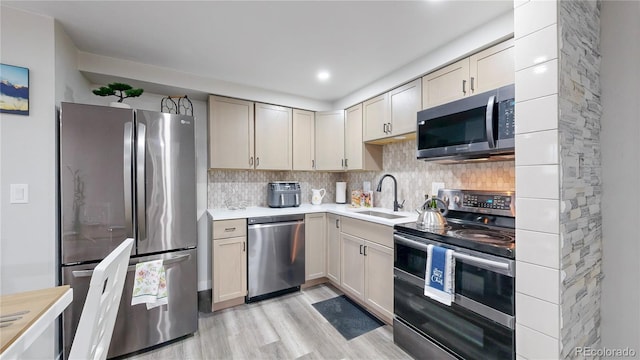 kitchen featuring stainless steel appliances, a sink, light countertops, light wood finished floors, and tasteful backsplash