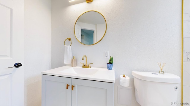 bathroom with toilet, a textured wall, and vanity