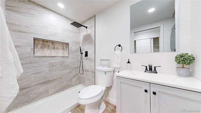 bathroom with recessed lighting, toilet, vanity, wood finished floors, and tiled shower