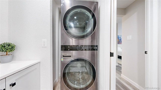 laundry area featuring laundry area, baseboards, stacked washing maching and dryer, and wood finished floors