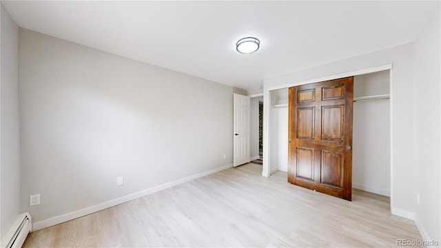 unfurnished bedroom featuring a baseboard radiator, a closet, light wood finished floors, and baseboards