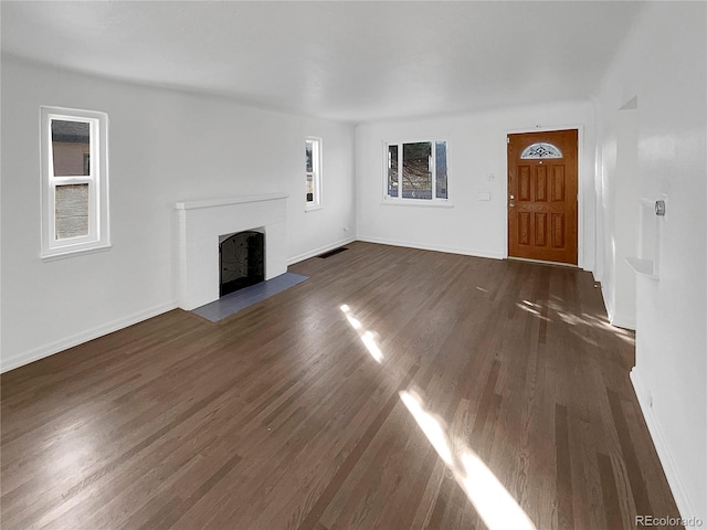 unfurnished living room with dark wood-style flooring, a brick fireplace, visible vents, and baseboards