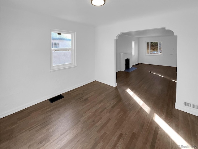 unfurnished living room featuring arched walkways, dark wood-style flooring, visible vents, and baseboards