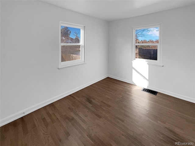 empty room with dark wood-style floors, baseboards, and visible vents