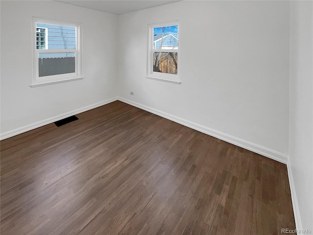 unfurnished room with dark wood-type flooring, visible vents, and baseboards