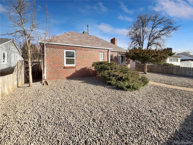 back of house featuring brick siding, a chimney, and fence