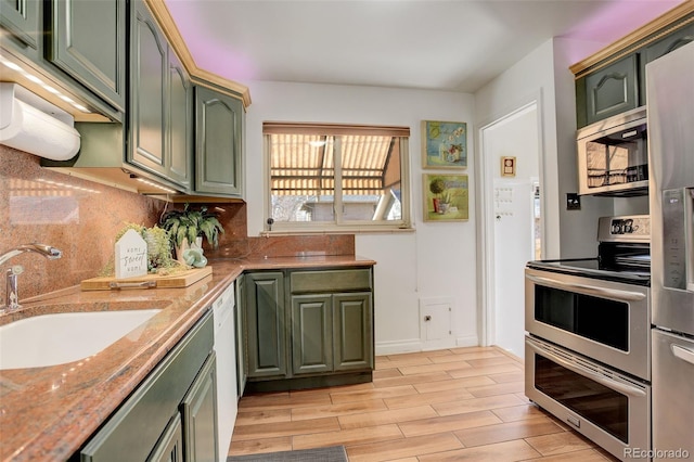 kitchen featuring sink, light hardwood / wood-style flooring, appliances with stainless steel finishes, tasteful backsplash, and green cabinetry