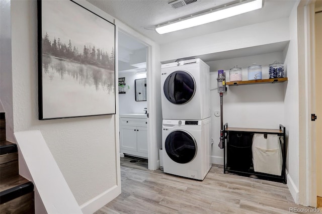 washroom featuring light hardwood / wood-style flooring, stacked washer and clothes dryer, and a textured ceiling