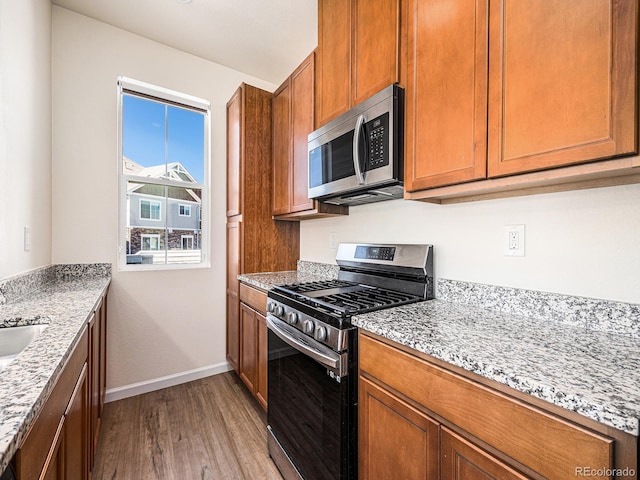 5755 S Buchanan Ct Unit E, Aurora, CO 80016 - kitchen featuring stainless steel appliances, light wood finished floors, brown cabinets, and light stone countertops