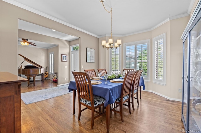 dining space with light wood-type flooring, a chandelier, baseboards, crown molding, and a ceiling fan