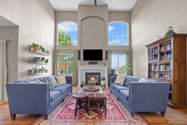 living room with a towering ceiling, plenty of natural light, wood finished floors, and a glass covered fireplace