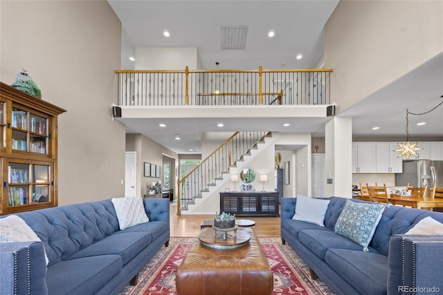 living room with stairs, light wood-type flooring, a towering ceiling, and recessed lighting
