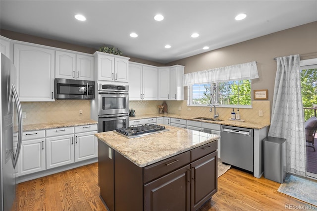 kitchen featuring stainless steel appliances, a sink, light wood-style floors, white cabinetry, and tasteful backsplash