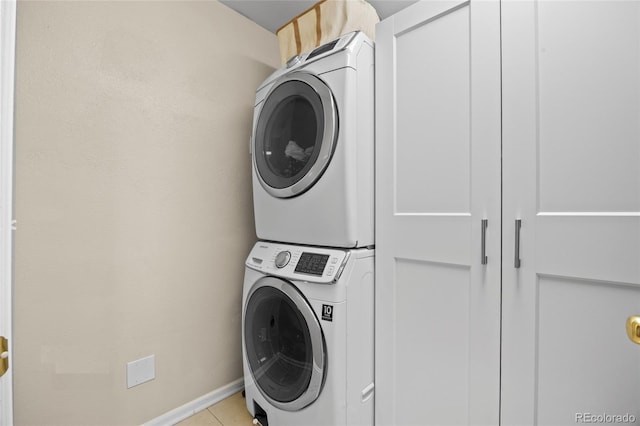washroom featuring stacked washing machine and dryer, light tile patterned flooring, and baseboards