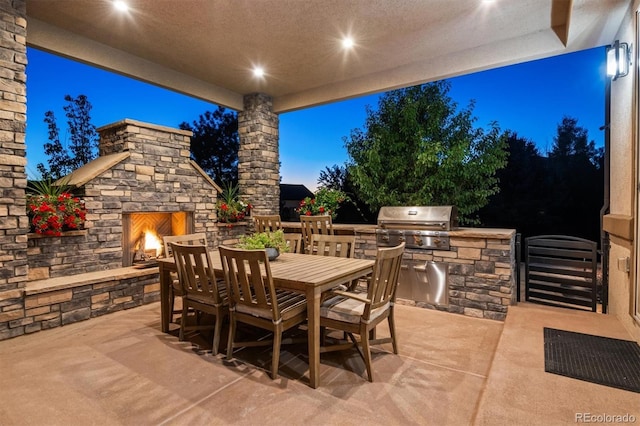 patio terrace at dusk featuring area for grilling, an outdoor stone fireplace, and exterior kitchen