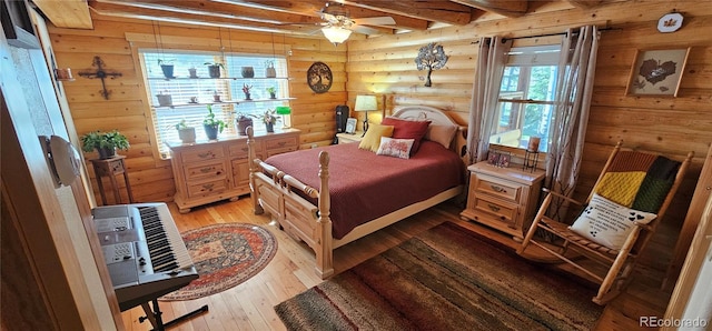 bedroom with log walls, beam ceiling, wood walls, and light wood-style flooring