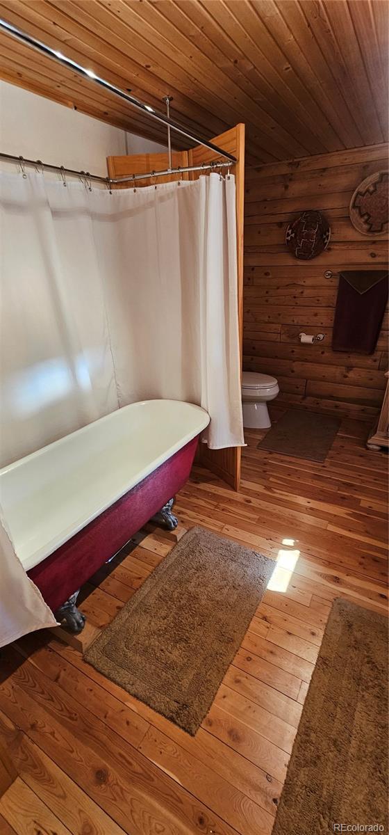 bathroom featuring log walls, toilet, wood finished floors, and wood ceiling