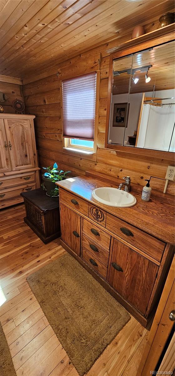 bathroom featuring a shower with shower curtain, wooden ceiling, wood finished floors, log walls, and vanity