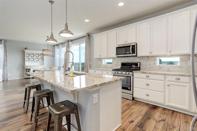11038 Unity Ln, Commerce City, CO 80022 - kitchen featuring stainless steel appliances, a kitchen breakfast bar, white cabinetry, wood finished floors, and recessed lighting
