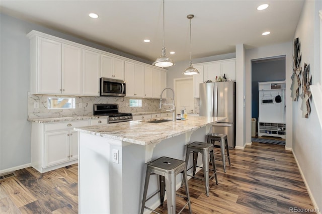 11038 Unity Ln, Commerce City, CO 80022 - kitchen with appliances with stainless steel finishes, backsplash, wood finished floors, a breakfast bar area, and white cabinets