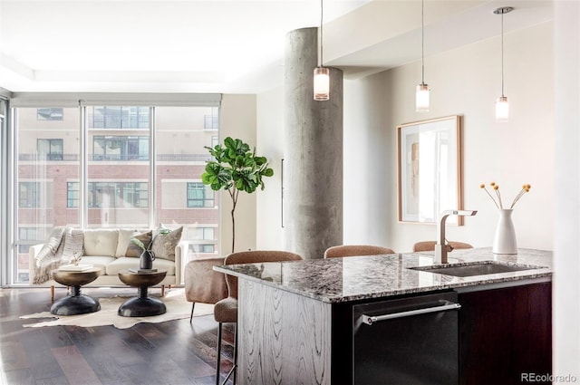 kitchen featuring a sink, dishwasher, a breakfast bar area, hanging light fixtures, and dark wood-style flooring