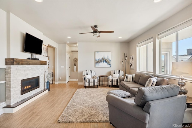 living area with ceiling fan, light wood finished floors, recessed lighting, a glass covered fireplace, and baseboards