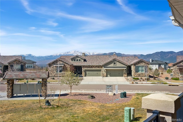 view of front facade featuring a mountain view, stone siding, concrete driveway, a garage, and a front yard