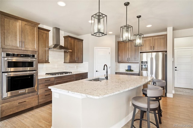 kitchen featuring a sink, wall chimney exhaust hood, stainless steel appliances, an island with sink, and tasteful backsplash
