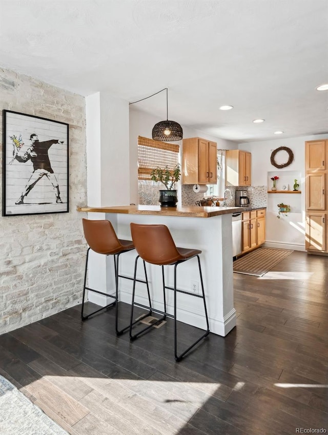 kitchen with a breakfast bar area, dark wood-style flooring, tasteful backsplash, stainless steel dishwasher, and a peninsula