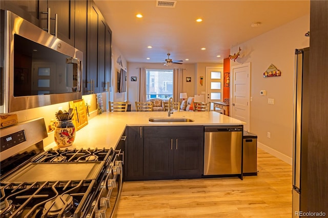 kitchen with stainless steel appliances, light wood-type flooring, kitchen peninsula, ceiling fan, and sink