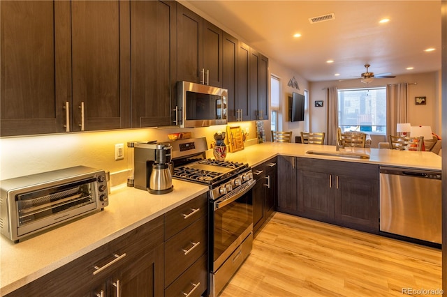 kitchen featuring sink, ceiling fan, light hardwood / wood-style floors, kitchen peninsula, and appliances with stainless steel finishes