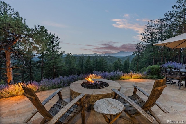 2929 Highlands View Rd, Evergreen, CO 80439 - patio terrace at dusk featuring a patio area, an outdoor fire pit, a wooded view, and a mountain view