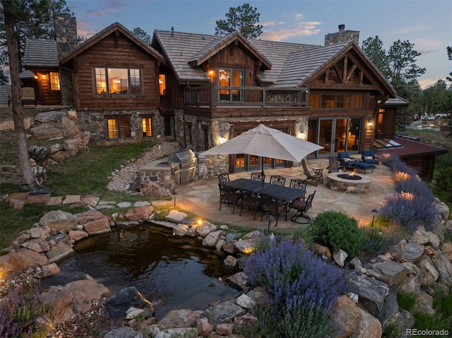 2929 Highlands View Rd, Evergreen, CO 80439 - back of property featuring an outdoor fire pit, a chimney, a balcony, a patio area, and an outdoor kitchen